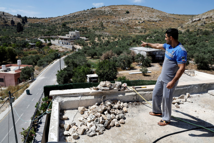 A Palestinian man points from a rooftop as he stands next to a stockpile of rocks which, according to the locals, are to be used for protection, following a spate of attacks by Israeli settlers, on a rooftop in the Palestinian village of Burqa