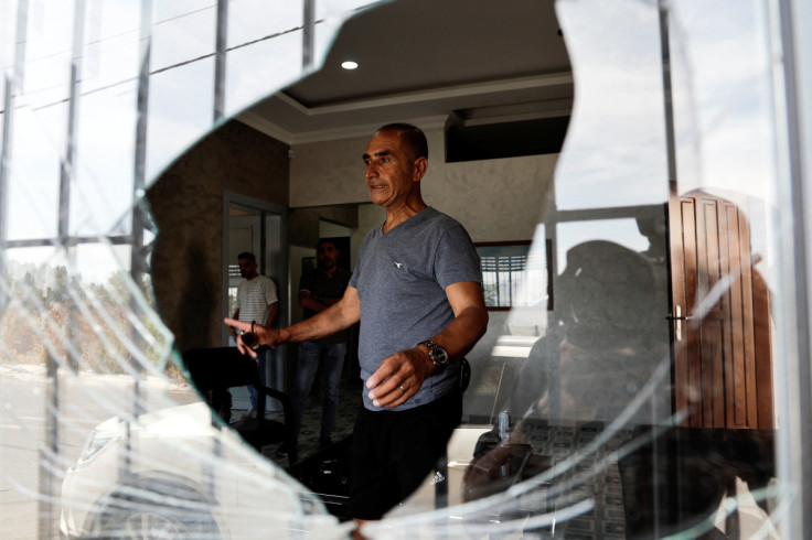 A Palestinian man is photographed through the broken window of his home after it was damaged in an attack by Israeli settlers in the Palestinian village of Burqa