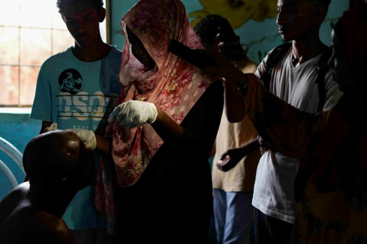 A Sudanese woman stitches up a head wound in Khartoum's sister city Omdurman under the light of a mobile phone