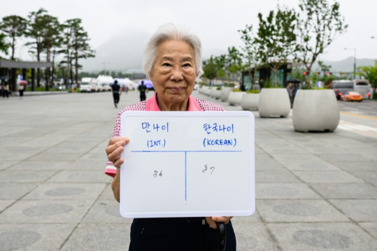 Lee Kyu-ok, poses with a whiteboard showing her international age, 86, and Korean age, 87