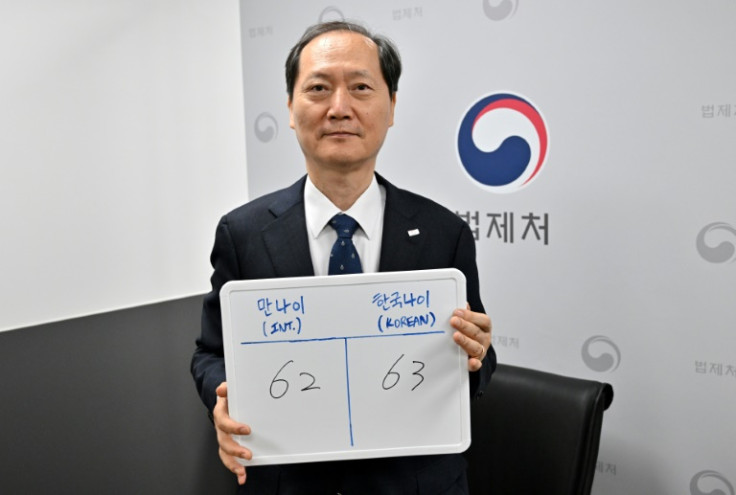 South Korea's Minister of Government Legislation Lee Wan-kyu, who is overseeing the official age change, holding a whiteboard with his Korean age (R) and his international age (L)