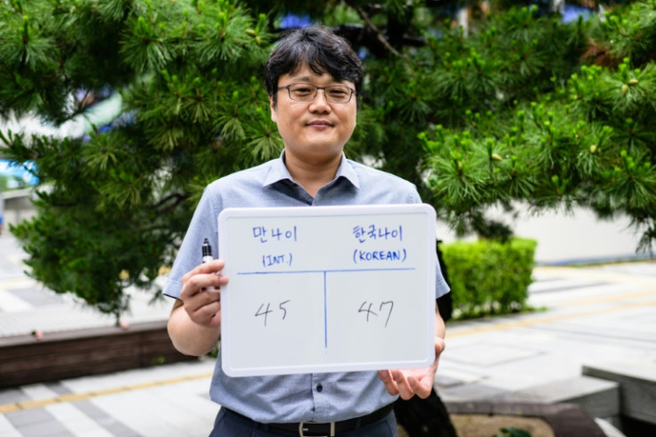 Hong Suk-min, an office worker, poses with a whiteboard showing his international age, 45, and Korean age, 47