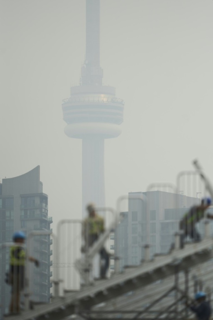 Workers assemble temporary grandstands for the Grand Prix of Toronto IndyCar series, as smoke from wildfires obscures the CN Tower in Toronto