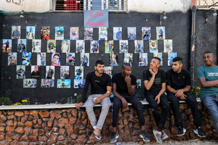 Men sit before a wall displaying pictures of killed Palestinians in Jenin