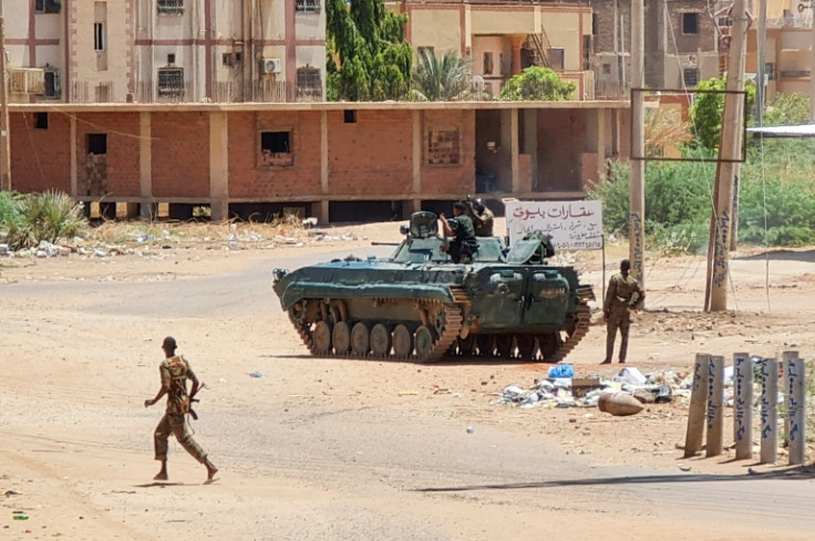 Sudanese Army sodliers walk near armoured vehicles stationed on a street in southern Khartoum on May 6, 2023