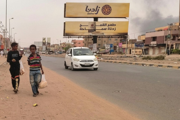 Smoke rises from nearby fighting as children take bags of bread home in Omdurman