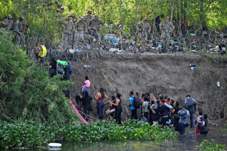 Migrants who crossed the Rio Bravo river (Rio Grande in the US) are stopped by members of the US National Guard reinforcing a barbed-wire fence along the US-Mexico border river in May 2023.