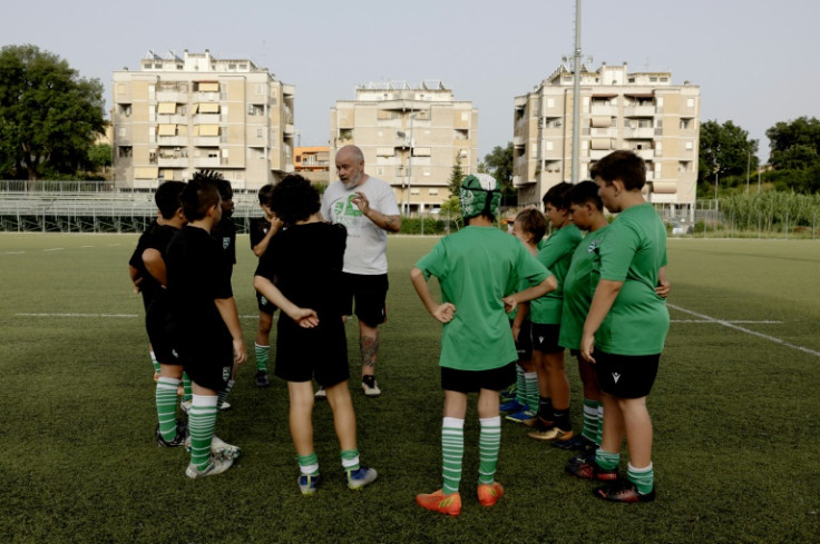 The young players at the Arvalia Villa Pamphili Rugby Roman club listen to their coach under the shadow of Corviale's massive housing project