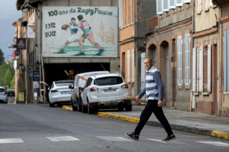 Former player Francis Sentenac crosses the road in front of a mural declaring '100 years of rugby passion' in Saint-Sulpice-sur-Leze