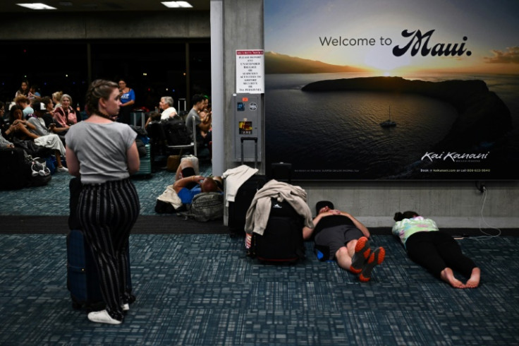 Passengers try to sleep below a 'Welcome To Maui' billboard on the floor of the airport terminal while waiting for evacuation flights off the island