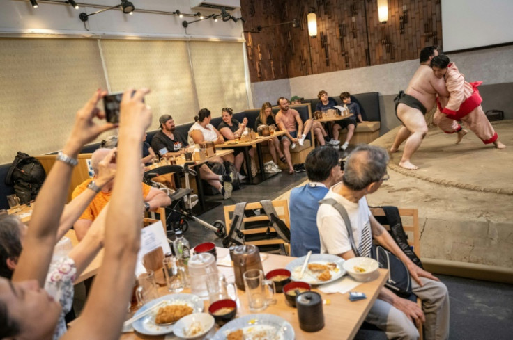 Diners watch as a foreign tourist (far R) wearing a costume tries to push a former sumo out of the ring