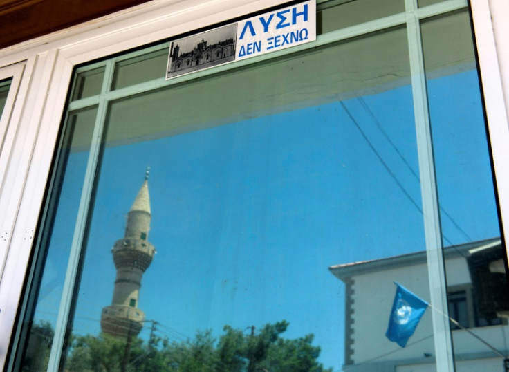 A mosque minaret and the United Nations flag are reflected on a door with a sign reading in Greek: 'Solution, I do not forget', in Pyla, a bi-communal village in the UN-patrolled buffer zone of Cyprus, in June 2017