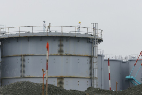 Workers wearing protective gear stand on a tank that stores radiation-contaminated water at Japan's Fukushima nuclear power plant in 2014