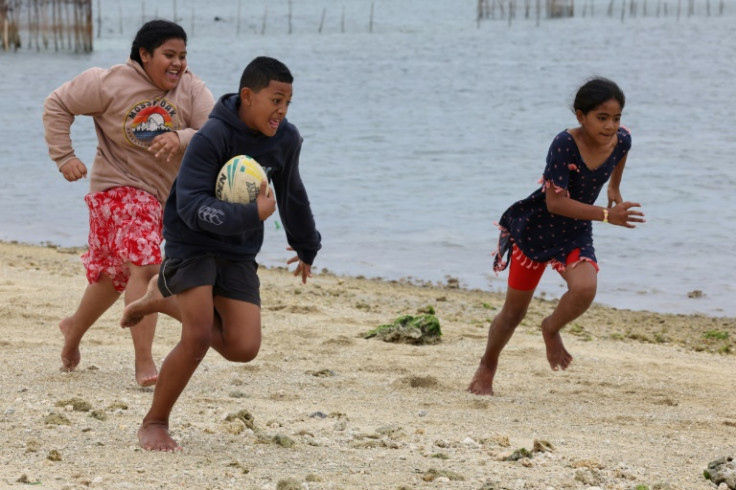 Siua (with ball), Sisi (left) and Lesieli (right) play touch on the beach in Popua as their families fish for dinner