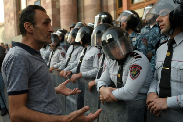 A protester speaks with Armenian police officers as they guard the entrance to the Government House in Yerevan