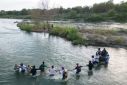 A group of migrants hold hands as they cross the Rio Grande river