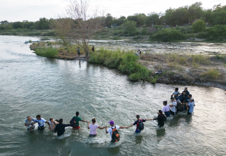 A group of migrants hold hands as they cross the Rio Grande river