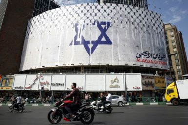 People drive past an anti-Israel billboard with the chequerred keffiye covering the Star of David in Tehran's central Vali-Asr square