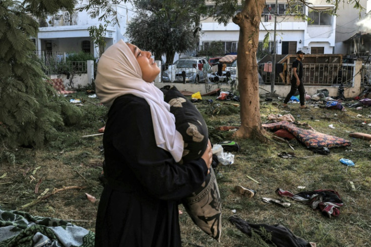 A woman reacts while holding a pillow as she stands amidst debris outside the site of the Ahli Arab hospital in Gaza City on October 18, 2023 in the aftermath of an overnight strike there.