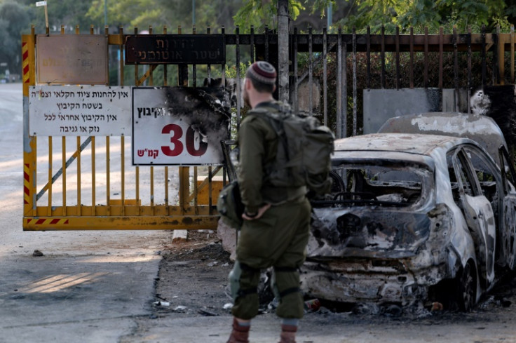 An Israeli soldier stands near a burnt car at the main entrance of Kibbutz Beeri on October 14, 2023