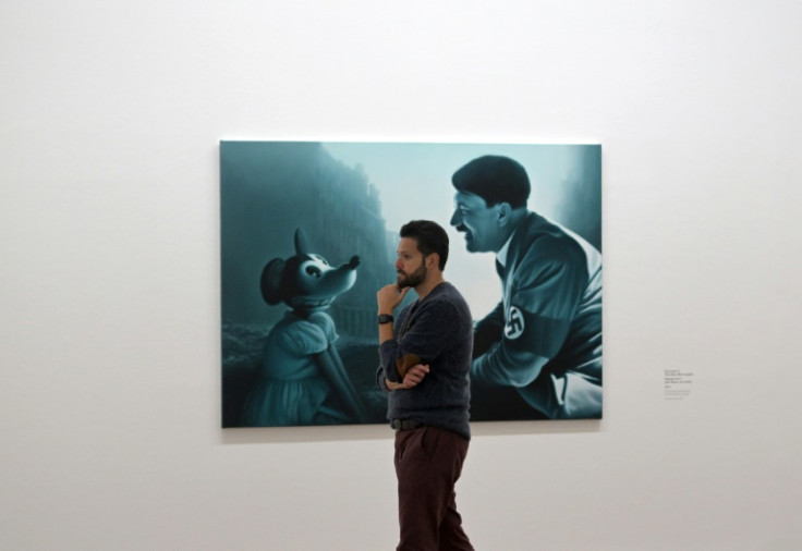 A visitor walks past a Helnwein painting called "Encounter 2 (The Man who Laughs)"