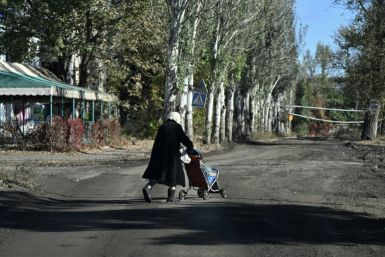 An elderly woman carries bottles of water in a child stroller down a street in the frontline town of Chasiv Yar in eastern Ukraine