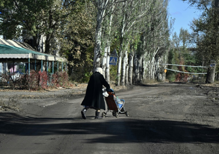 An elderly woman carries bottles of water in a child stroller down a street in the frontline town of Chasiv Yar in eastern Ukraine