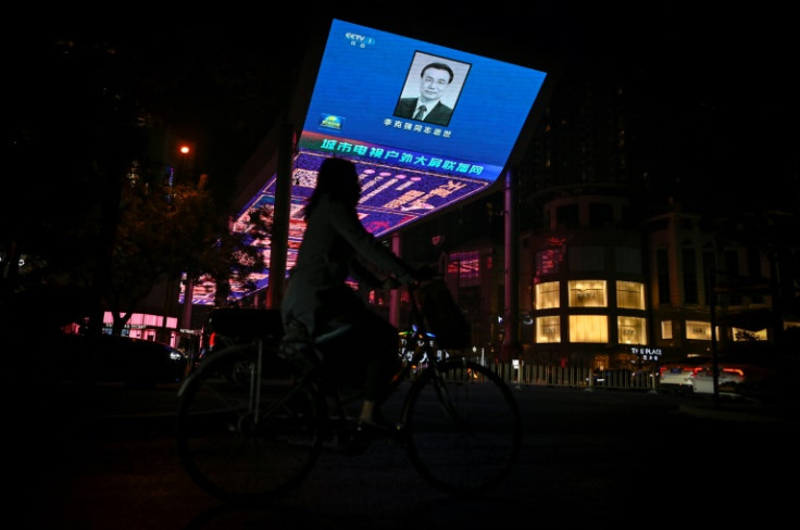 A woman rides a bicycle past a screen broadcasting an obituary of the former Chinese premier Li Keqiang outside a mall in Beijing