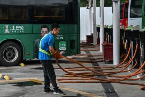 A worker holds a charging cable next to electric buses at Antuoshan charging station in Shenzhen, China