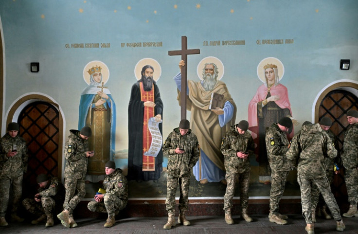 Ukrainian servicemen look their smartphones as they wait, shelting from the autumn rain as they stand next to murals in a cathedral in Kyiv