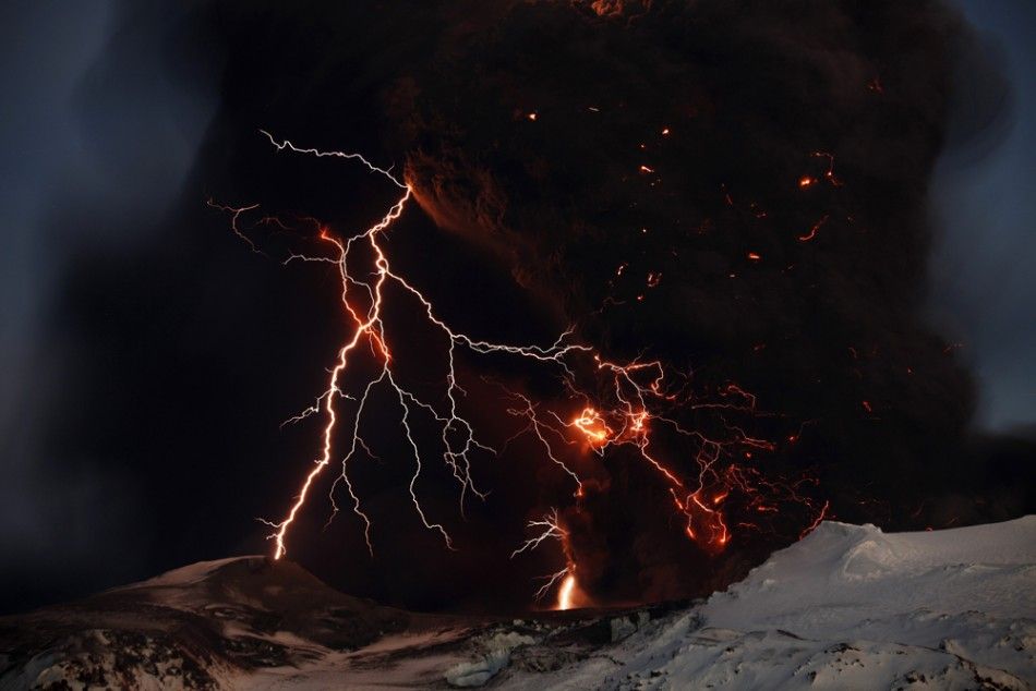Lightning streaks across the sky as lava flows from a volcano