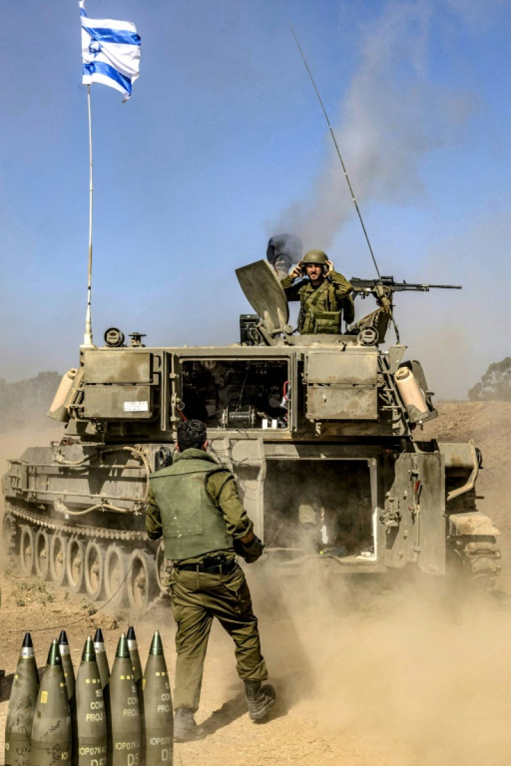 An Israeli soldier carries rounds from a stockpile towards a stationed self-propelled artillery howitzer firing from a position near the border with the Gaza Strip in southern Israel on November 6, 2023