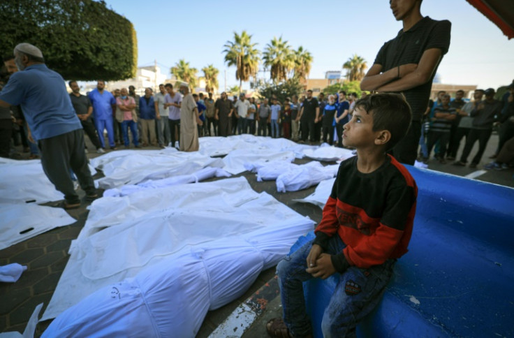 A Palestinian child sits next to bodies of those killed in Israeli bombardment, prior to the corpses being taken from the Shuhada Al-Aqsa hospital for burial, in Deir el-Balah, in the central Gaza Strip on November 6, 2023
