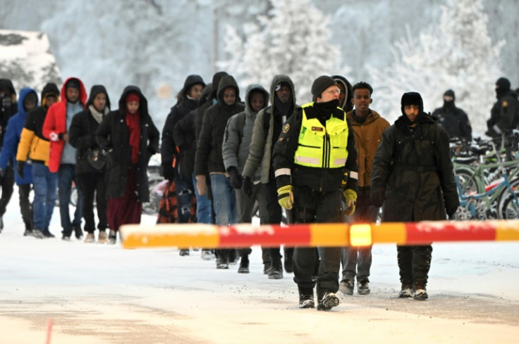 A Finnish border guard escorts migrants at the border with Russia