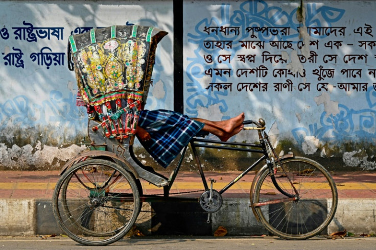 A bicycle rickshaw driver rests in his vehicle by a street kerb in Dhaka