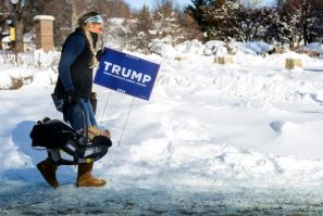 A supporter of former US President and 2024 presidential hopeful Donald Trump carries a baby and a Trump placard as she braves the below zero temperatures to attend a rally in Indianola, Iowa, on January 14, 2024