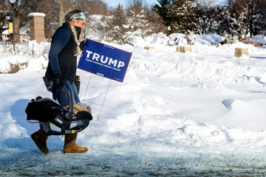 A supporter of former US President and 2024 presidential hopeful Donald Trump carries a baby and a Trump placard as she braves the below zero temperatures to attend a rally in Indianola, Iowa, on January 14, 2024