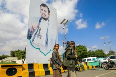 Yemeni fighters walk past a large portrait of Huthi leader Abdulmalik al-Huthi on a street in Sanaa