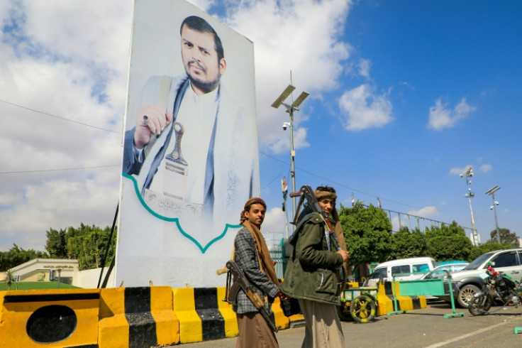Yemeni fighters walk past a large portrait of Huthi leader Abdulmalik al-Huthi on a street in Sanaa