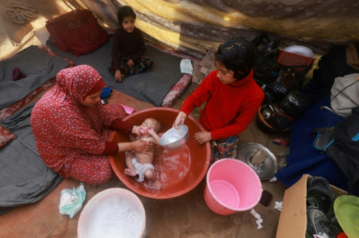 A woman gives a baby a bath inside a tent at a camp for displaced Palestinians in Rafah in the southern Gaza Strip