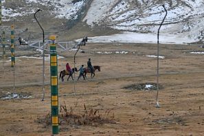 A guide leads horses along a path near ski slopes usually covered in snow in Gulmarg