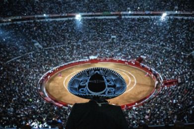 A man wearing a traditional hat watches a bullfight at the Plaza de Toros in Mexico City