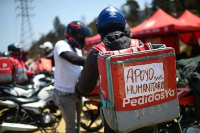 Venezuelans who work for online food delivery services and have motorbikes, pasted signs reading "humanitarian aid" to their backpacks, carrying water and food to the neighborhoods where they often work
