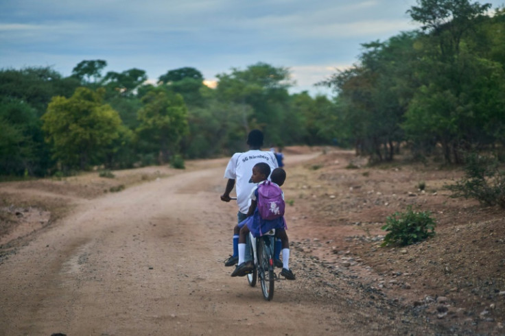 A relative pedals two students to school safely on a donated bicycle near Zimbabwe's Hwange National Park