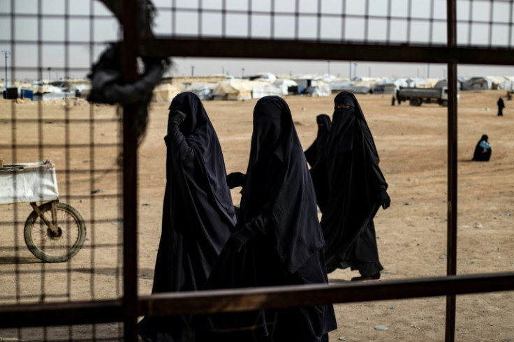 Women in niqabs walk past a fence at the al-Hol camp in Syria where thousands of families of Islamic State fighters are still held