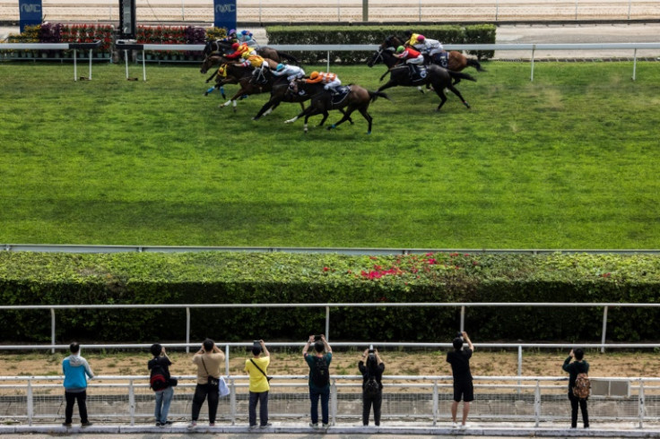 A handful of spectators watch horses flash past the finish line at one of the final Macau race meetings