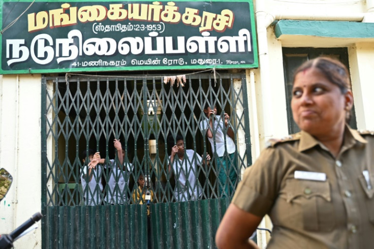 Students look through a school gate as a policewoman stands guard during an election campaign rally in Madurai