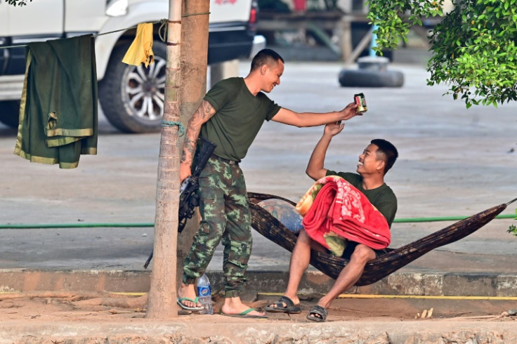 A member of a Myanmar militia holds a beer can and a weapon while talking to a comrade across the Moei river on the Myanmar side, as seen from Thailand's Mae Sot district
