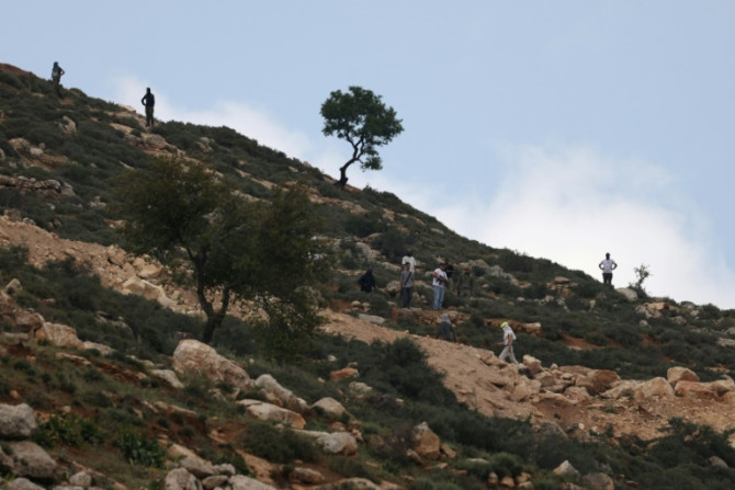 Armed Israeli settlers gather on a hill overlooking Al-Mughayyir village