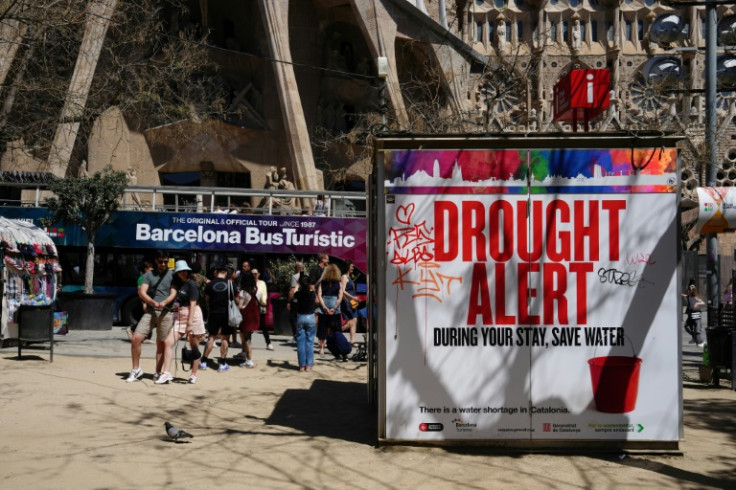 A couple uses a selfie stick to take a picture next to a banner warning tourists about a drought alert in Catalonia